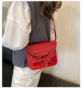 Model wearing a red patent leather shoulder bag with a bow accent and flap closure