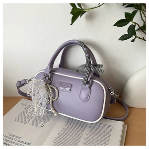 Détail du sac bowling lilas avec nœud à carreaux et pendentif perle sur un magazine