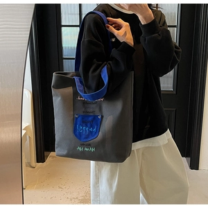 Detailed view of the canvas tote bag showing the blue pocket and embroidered letters