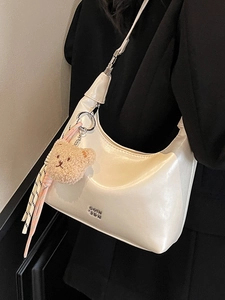 Minimalist white crescent dumpling bag with metallic logo and cute plush bear accessory