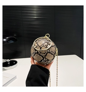 Detail of spherical evening bag with snakeskin texture and gold ring handle held by hand