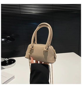 Detail of beige textured leather shell bag showing double handles and gold bead chain strap