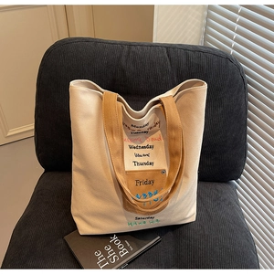 Detail of canvas tote bag showing embroidered letters and brown pocket on beige fabric