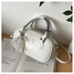Sac Boston blanc avec ruban à carreaux et pendentif en perles sur une table en bois naturel