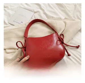 Dettaglio borsa a secchiello in pelle rossa con nodi laterali e logo in rilievo
