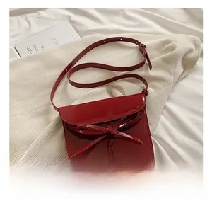 Detailed close-up of a glossy red oil wax leather envelope bag with a stylish bow decoration