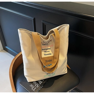 Close-up of beige canvas tote bag with brown straps and embroidered lettering