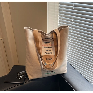 Detail of canvas tote bag with embroidered weekly letters and contrasting brown trim handles