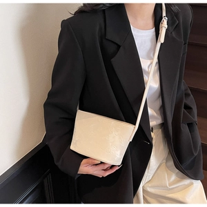 Détail du motif gaufré crème sur le sac seau brillant porté par un mannequin chic