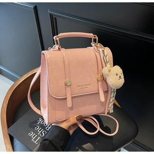 Detailed close-up of a pink textured leather mini backpack with a beige plush bear charm
