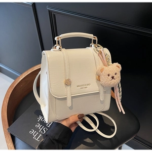 Close-up of white mini backpack with pebble leather texture and bear charm detail