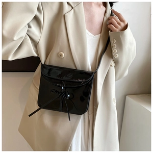 Detail of black glossy leather crossbody bag with bow decoration on a beige blazer model