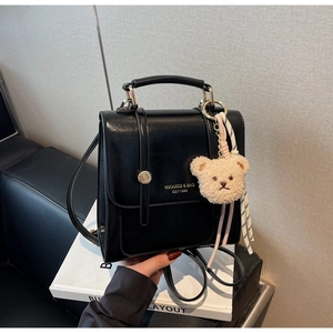 Detail of black PU leather bag with gold hardware and a cute plush bear charm accessory