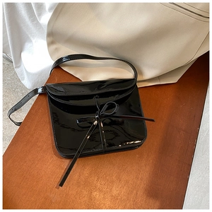 Macro shot of black patent leather shoulder bag with bow detail on a wood surface