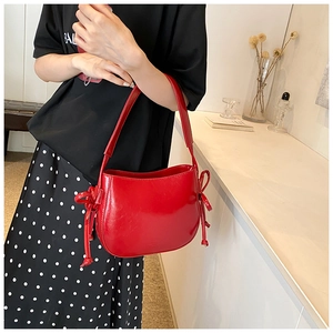 Dettaglio di una borsa a secchiello in pelle lucida rossa con fiocchi e tracolla