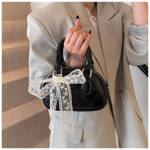 Close-up of black embossed Boston bag with a large white lace bow on the handle