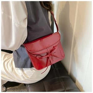 Detail view of red glossy patent leather shoulder bag featuring a stylish 3D bow decoration