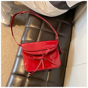 Detailed close-up of a red oil wax leather ballet bag with a delicate bow on a dark stool