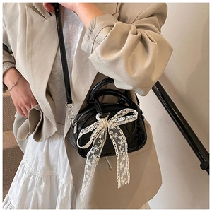 Detail of black mini Boston bag with embossed patterns and a white lace bow decoration