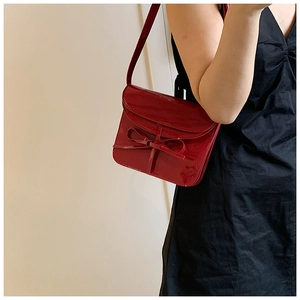 Detail of red oil wax leather envelope bag with ribbon bow on a minimalist crossbody strap