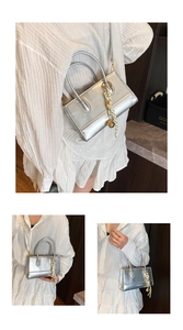 Detailansicht einer silbernen kleinen Tasche mit Fashion-Schriftzug und gestreiftem Seidenschal