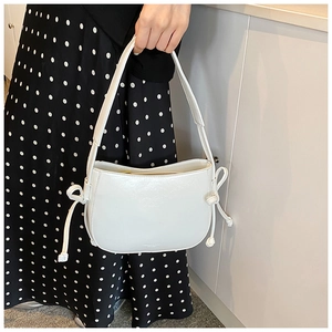 Dettaglio della borsa hobo bianca in pelle cerata con fiocchi su un abito a pois