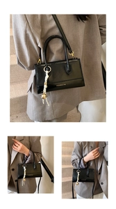 Detailansicht einer schwarzen glänzenden quadratischen Handtasche mit goldenem Logo