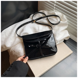 Close-up of black oil wax leather crossbody bag with bow detail on a beige book