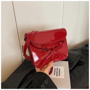 Detail of red oil wax leather crossbody bag featuring a chic bow and glossy finish