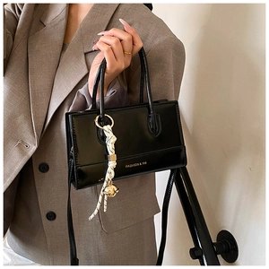 Detail der glänzenden schwarzen Handtasche mit goldenem Glockenanhänger und Fashion YM