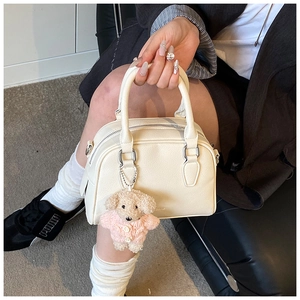 Detail view of cream leather bowling bag with lychee texture and cute plush puppy charm