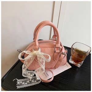 Detail of pink embossed mini Boston bag with lace bow pendant on wood tray