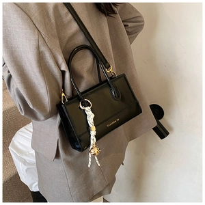 Detail einer schwarzen Glanztasche mit Goldlogo und dekorativem Glockenanhänger