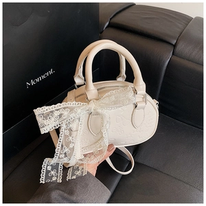 Detailed close-up of cream Boston bag with embossed patterns and lace bow decoration