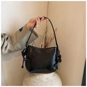 Dettaglio borsa a secchiello nera lucida con manici a nodo decorativo su piedistallo bianco