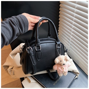 Detail of black pebbled leather bowling bag with cute plush puppy charm and zipper