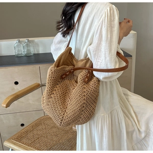 Close-up of woven straw tote bag featuring brown leather straps and detailed X-shaped stitching