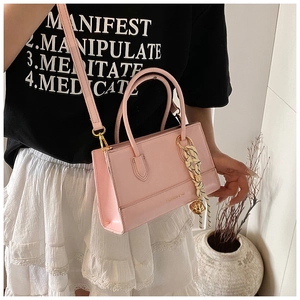 Detailansicht der rosa Ledertasche mit Doppelgriffen und geflochtenem Glockenanhänger
