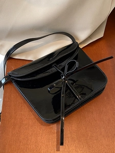 Glossy black oil wax leather ballet style crossbody bag with bow detail on wood surface