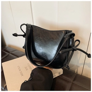 Dettaglio della borsa a secchiello in pelle nera lucida con nodi decorativi