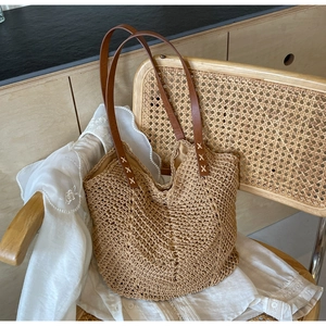 Detail of brown leather handles with cross-stitch sewing on a beige woven straw tote bag