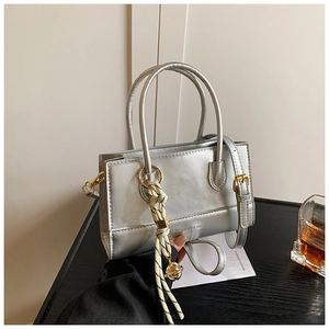 Detail der silbernen Metallhandtasche mit gewebtem Seilanhänger und Goldkugel auf dunklem Holz