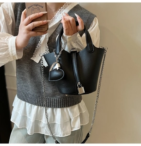 Detail of black pebbled leather bucket bag with silver lock and heart charm accessory