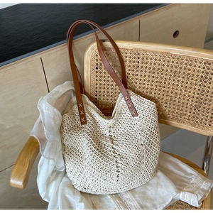 Detail of woven straw tote bag with brown leather straps and cross-stitch craft