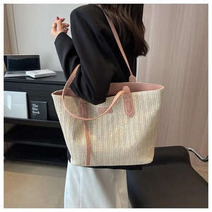 Close-up of woven straw tote bag featuring pink leather handles and gold logo detail