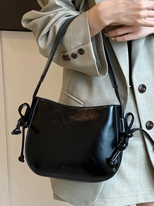 Borsa a secchiello in pelle cerata nera minimalista indossata con un blazer grigio chiaro