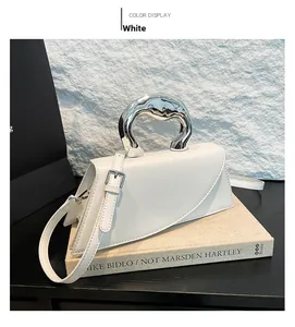 Sac carré blanc chic avec poignée en métal liquide argenté sur des livres d'art