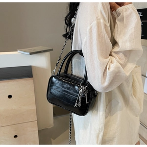 Dettaglio della borsa nera lucida con cuciture trapuntate e ciondoli a chiave argento