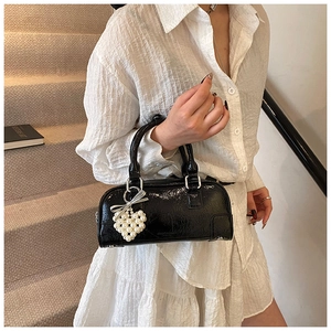 Close-up of black glossy mini pillow bag with silver bow and pearl heart charm detail