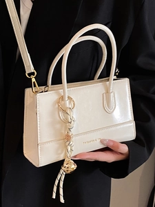 Elegante beige quadratische Handtasche für Damen mit goldenem Schriftzug auf schwarzem Blazer